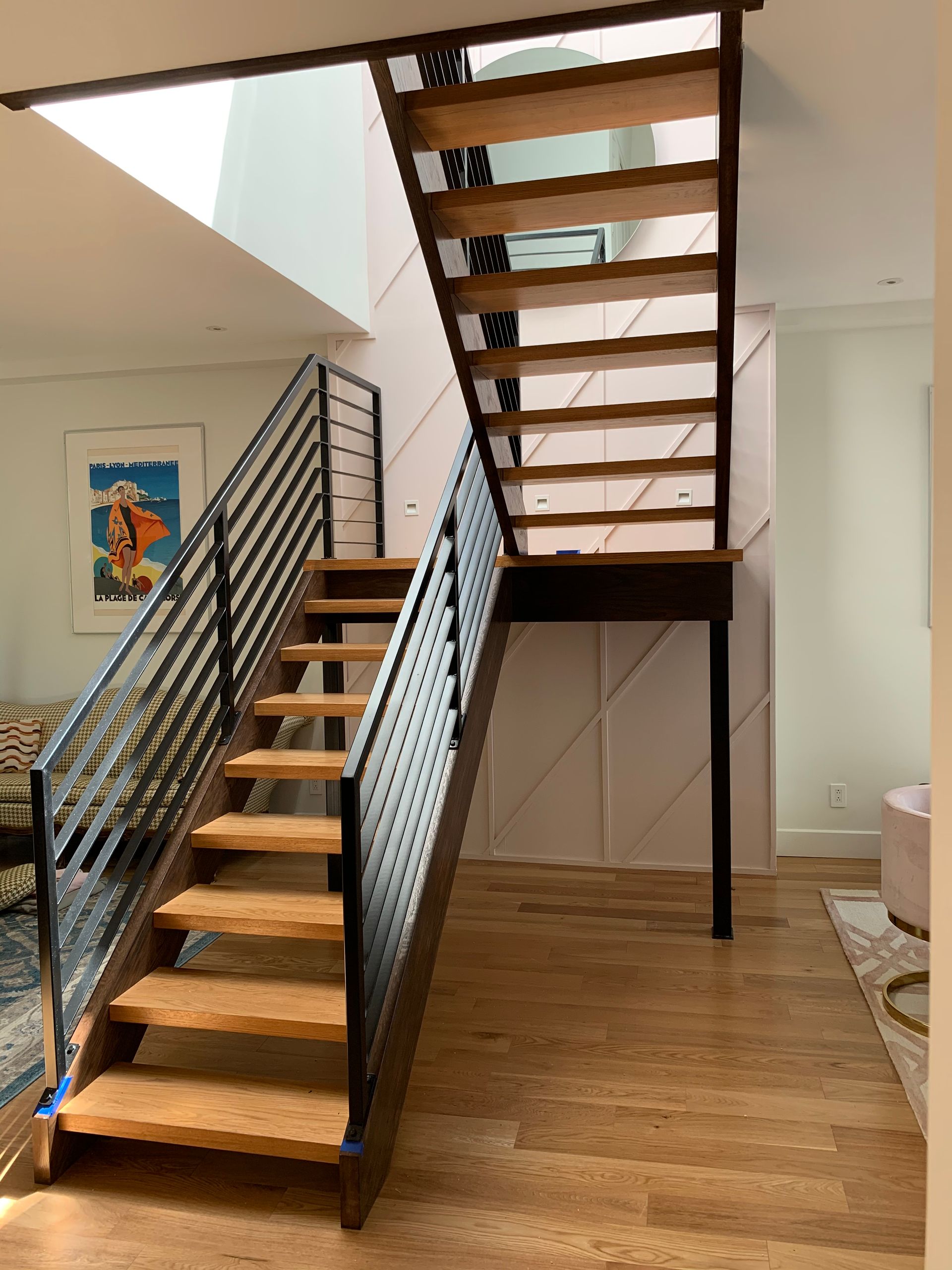 Escalier en bois avec rampe en métal noir dans une maison moderne. Lumière du soleil filtrant par un puits de lumière.