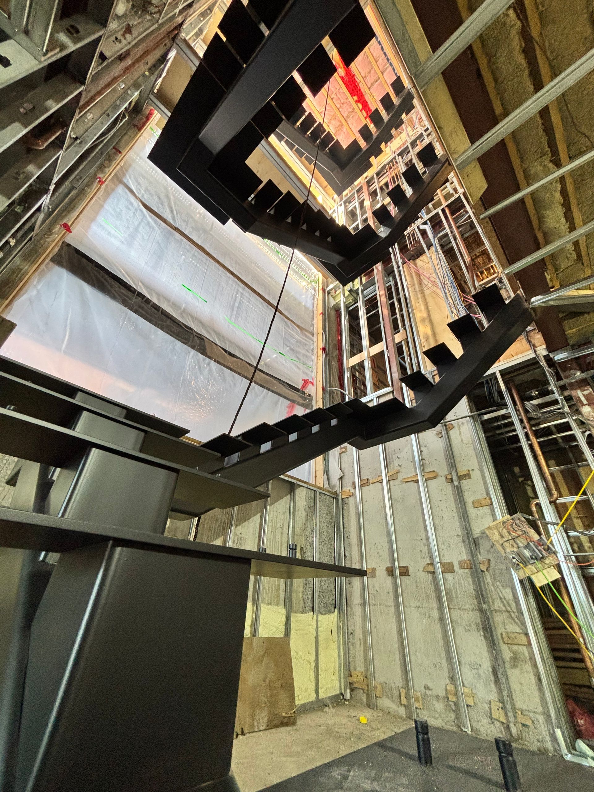 Intérieur d'un chantier de construction montrant un escalier en acier noir, des murs inachevés et la structure du bâtiment.