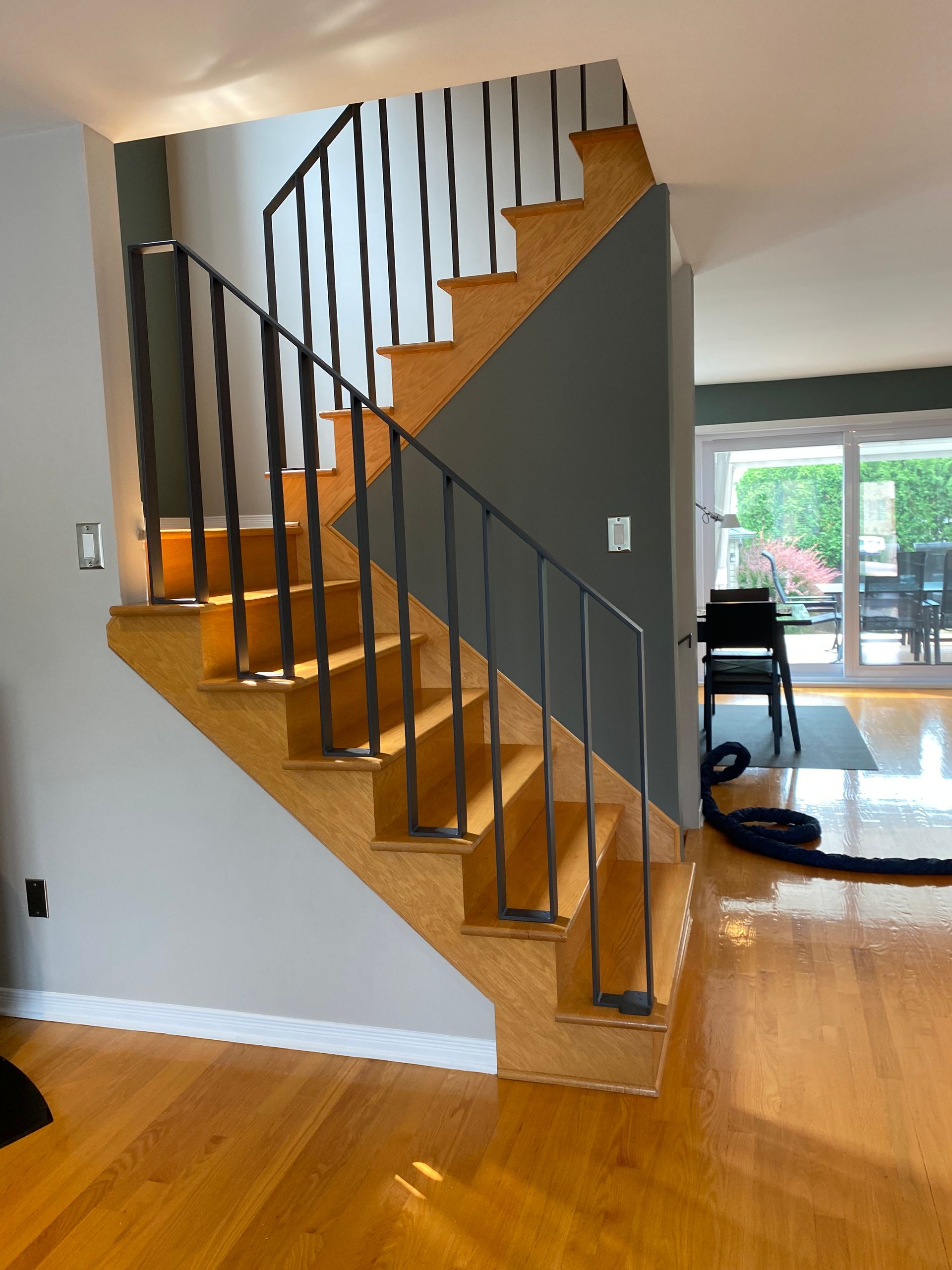 Escalier en bois avec rampe en métal noir, murs gris et parquet.