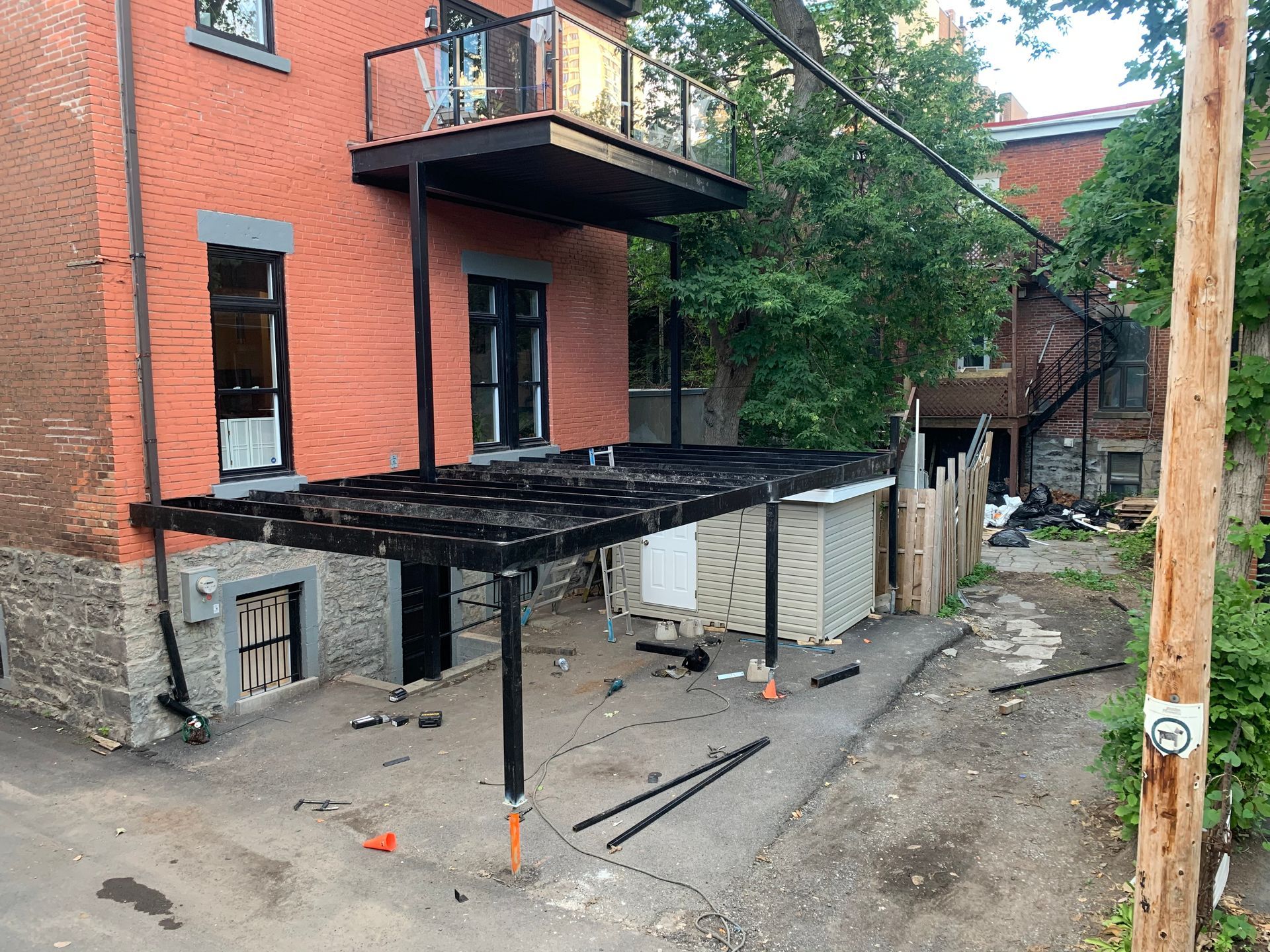 Bâtiment en briques avec structures métalliques noires, comprenant un balcon et un abri voiture ; vue extérieure.