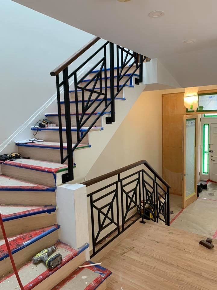 Escalier avec rampe en métal noir moderne et mains courantes en bois, menant à un niveau supérieur. Matériaux de construction présents.