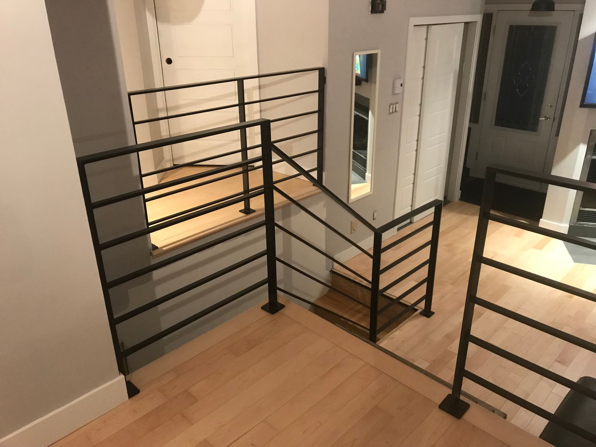 Rambarde en métal noir dans une maison, sur un parquet près d'un escalier.