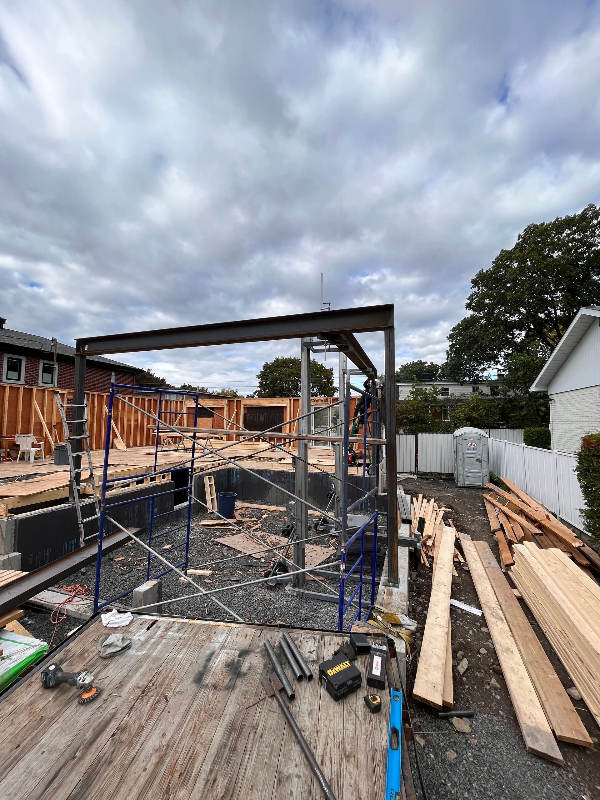 Chantier : charpente métallique et ossature bois, ciel couvert, pile de bois.
