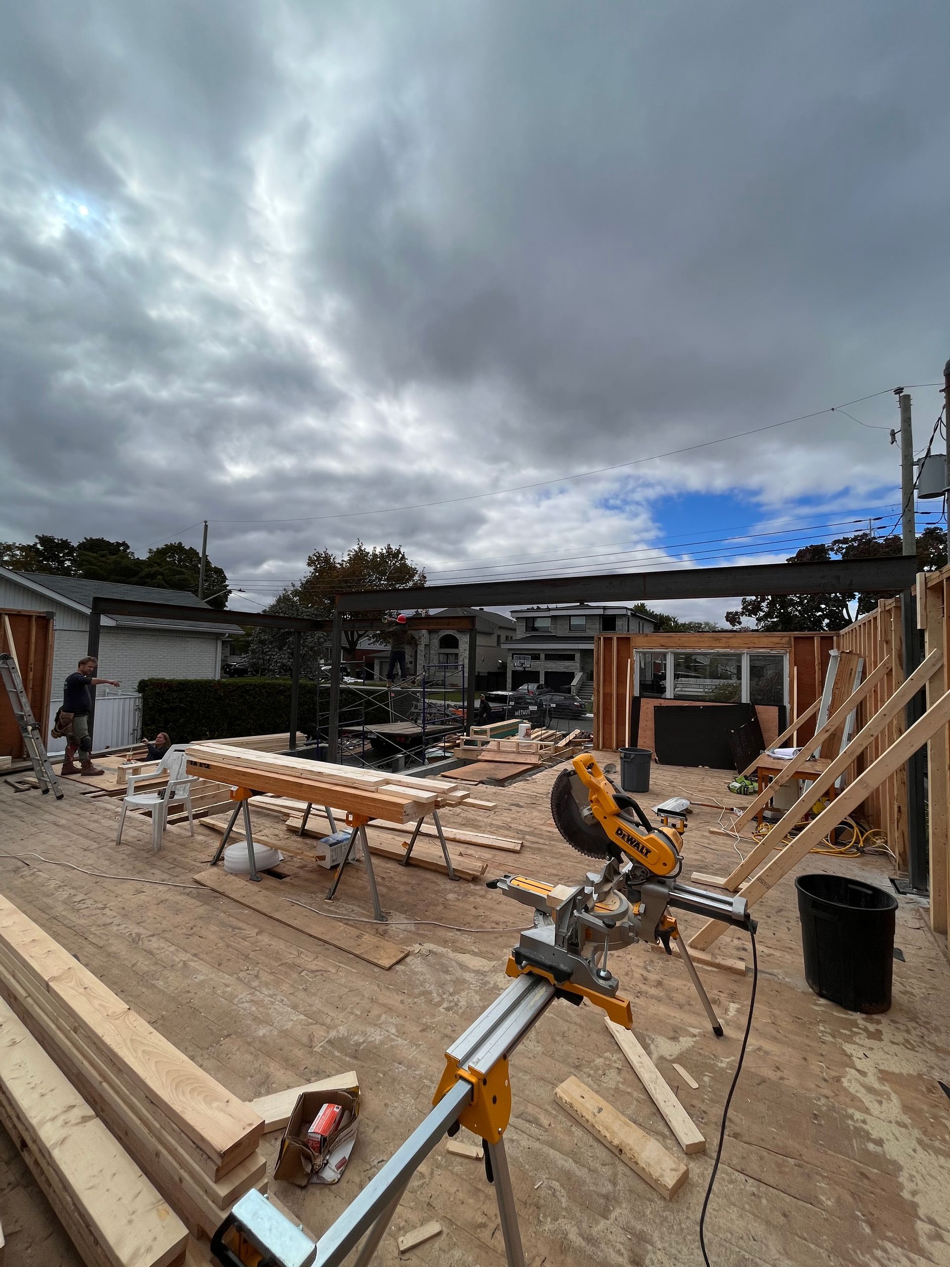 Chantier de construction avec du bois et une scie électrique sous un ciel nuageux.