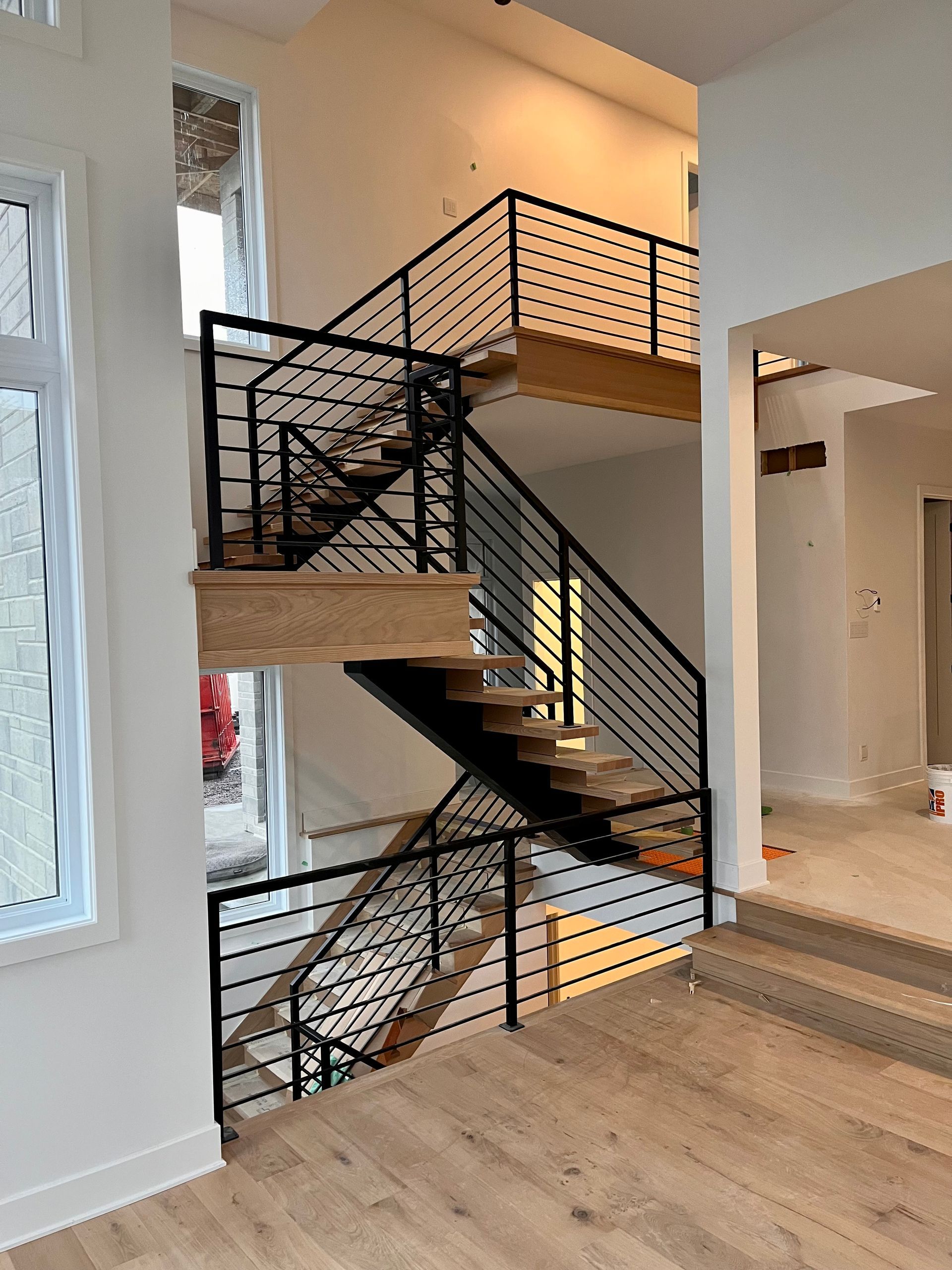Escalier à deux étages avec rampes en métal noir et marches en bois dans une maison neuve au sol clair.