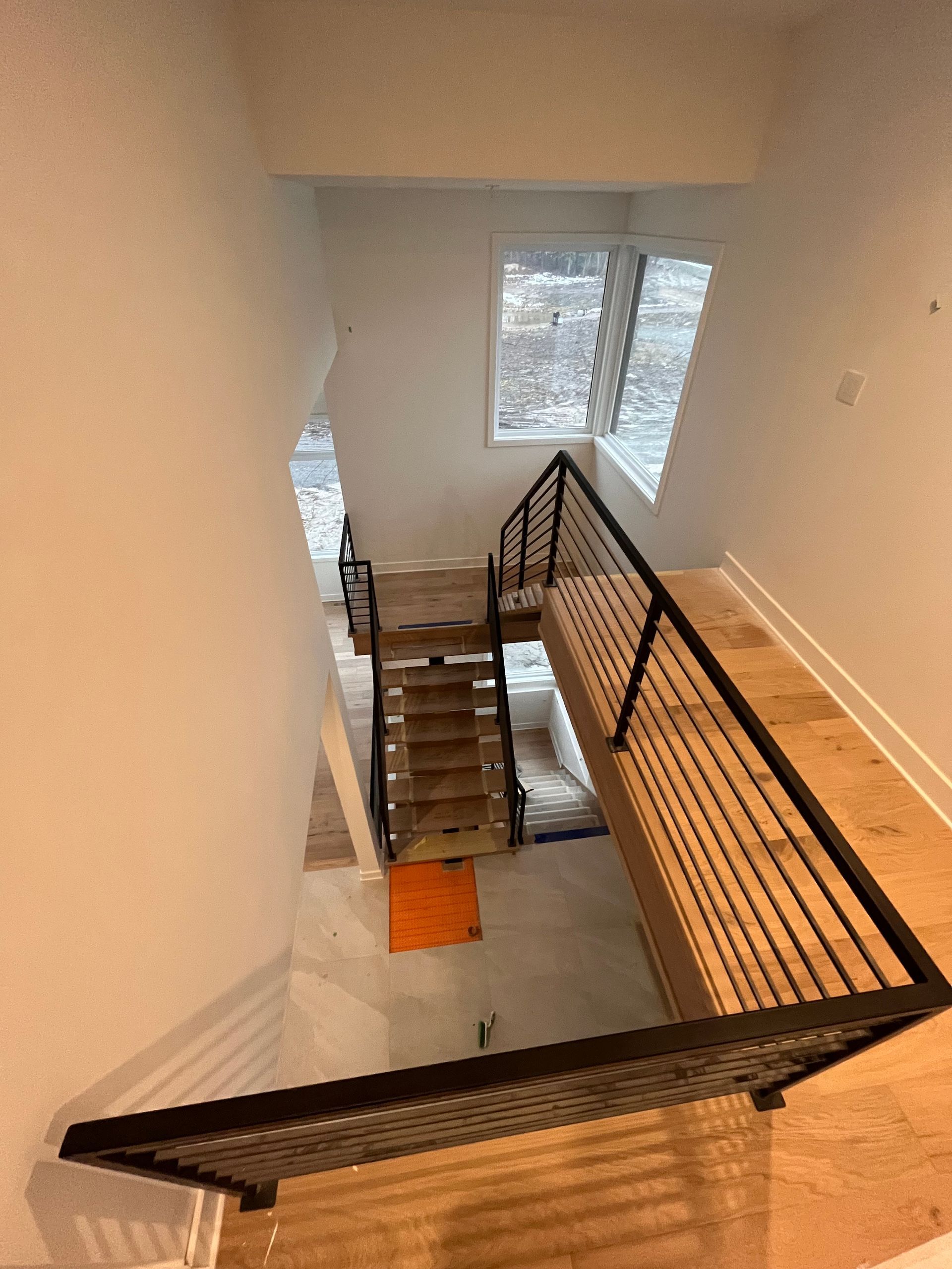 Escalier avec marches en bois et rampes en métal noir, descendant d'un palier au sol en bois clair.