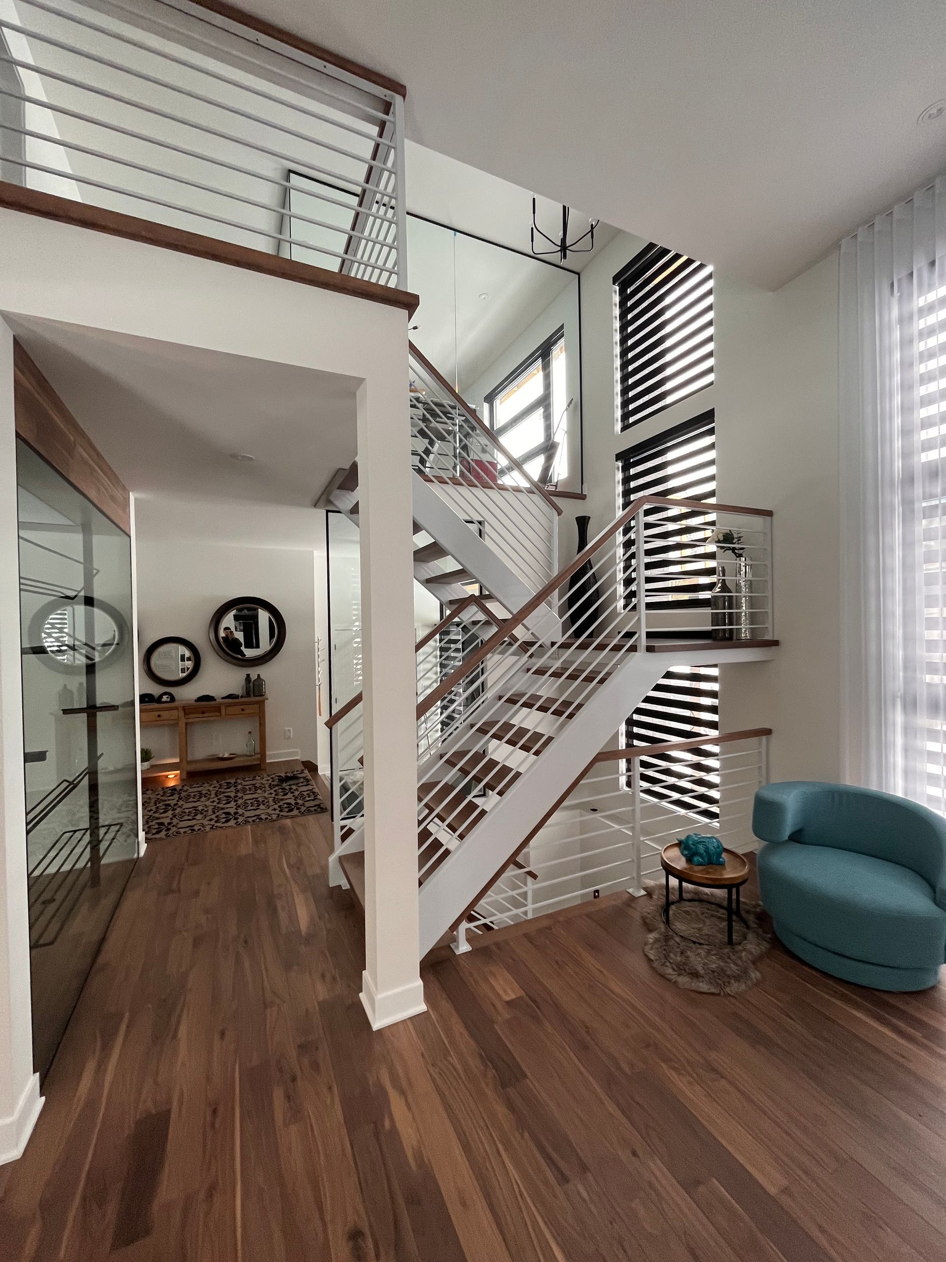 Vue intérieure d'une maison moderne avec un escalier, un parquet et un fauteuil bleu.