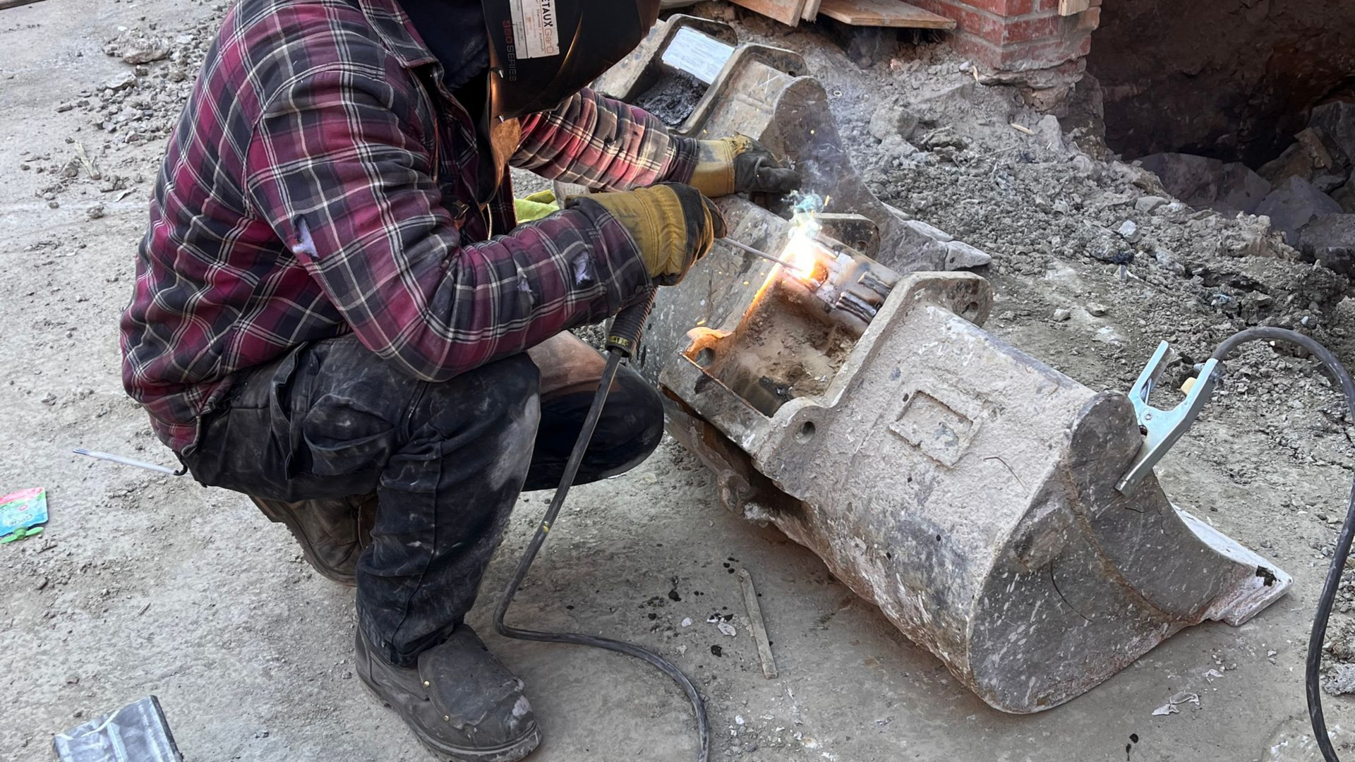 Un soudeur portant un masque travaille à l'extérieur sur un seau métallique sale.