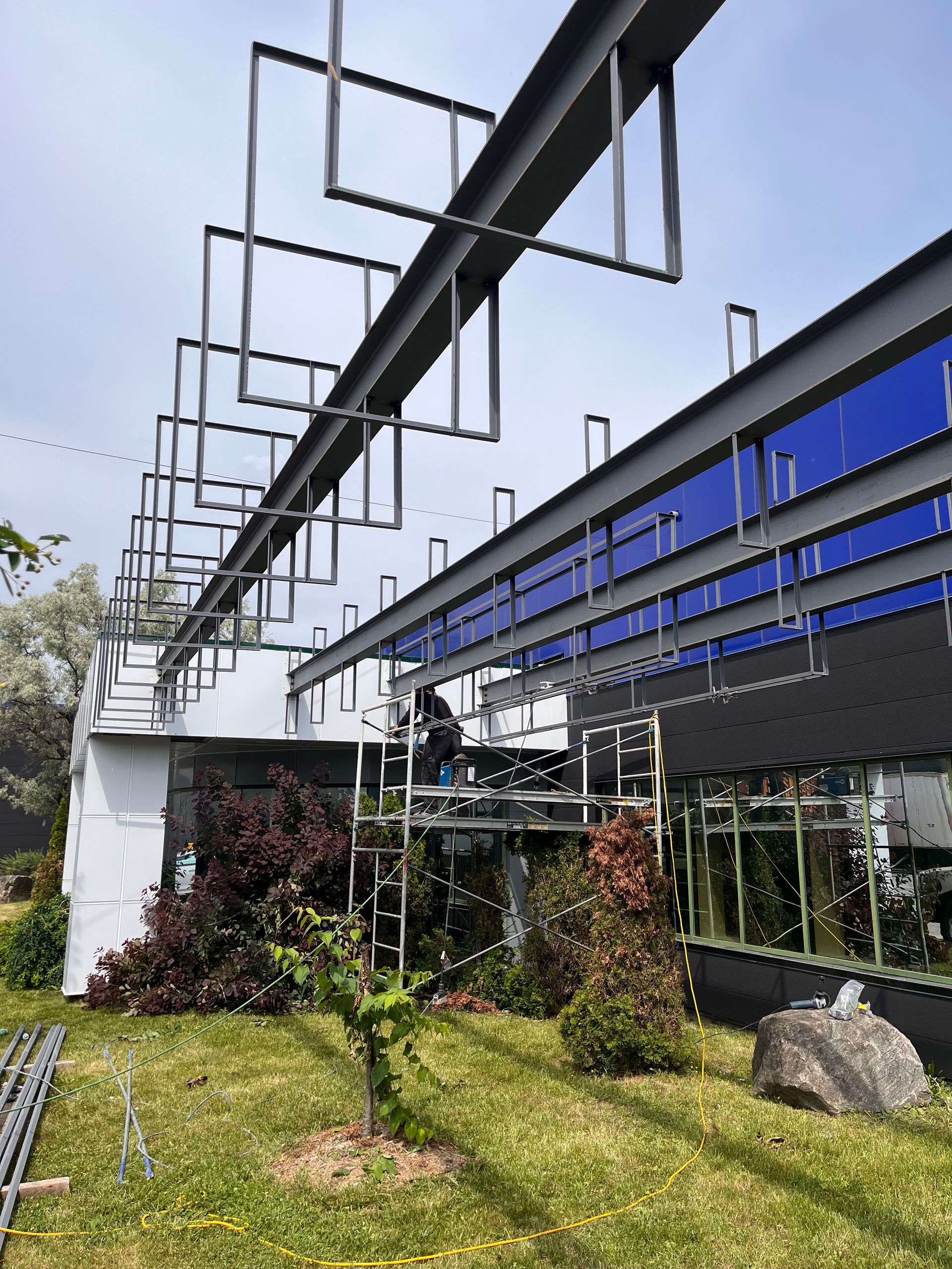 Une structure métallique s'étend depuis un bâtiment aux fenêtres bleues. Une personne travaille sur un échafaudage à l'extérieur.