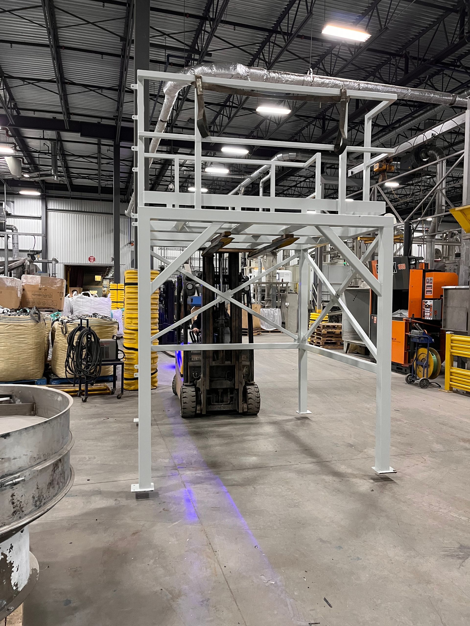 Structure industrielle en métal blanc avec un chariot élévateur à l'intérieur d'une usine.