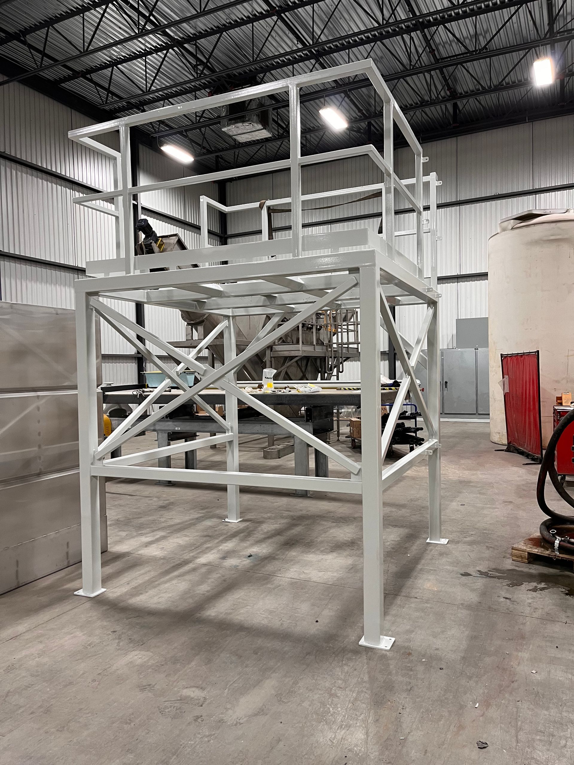 Plateforme industrielle en métal blanc avec escalier et rambarde à l'intérieur d'un entrepôt.