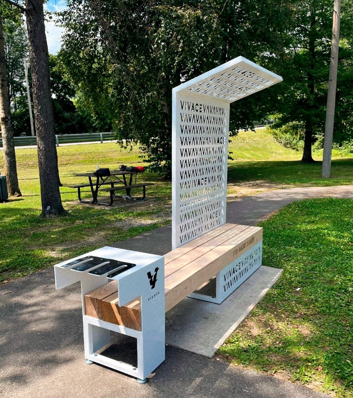 Banc de parc avec panneaux solaires, abri à motifs et table intégrée ; dans un cadre de parc.