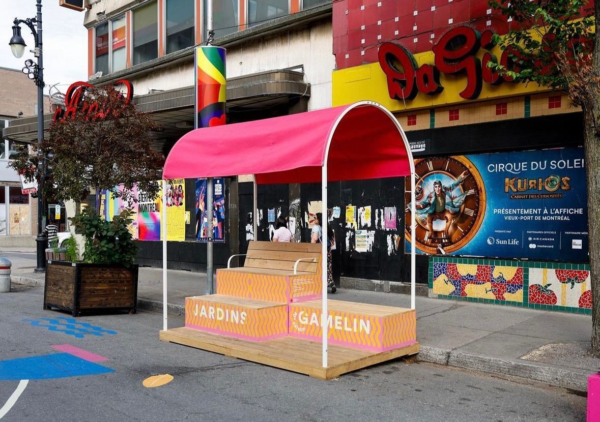 Un auvent rose recouvre un stand dans une rue de la ville. Un théâtre se dresse en arrière-plan.