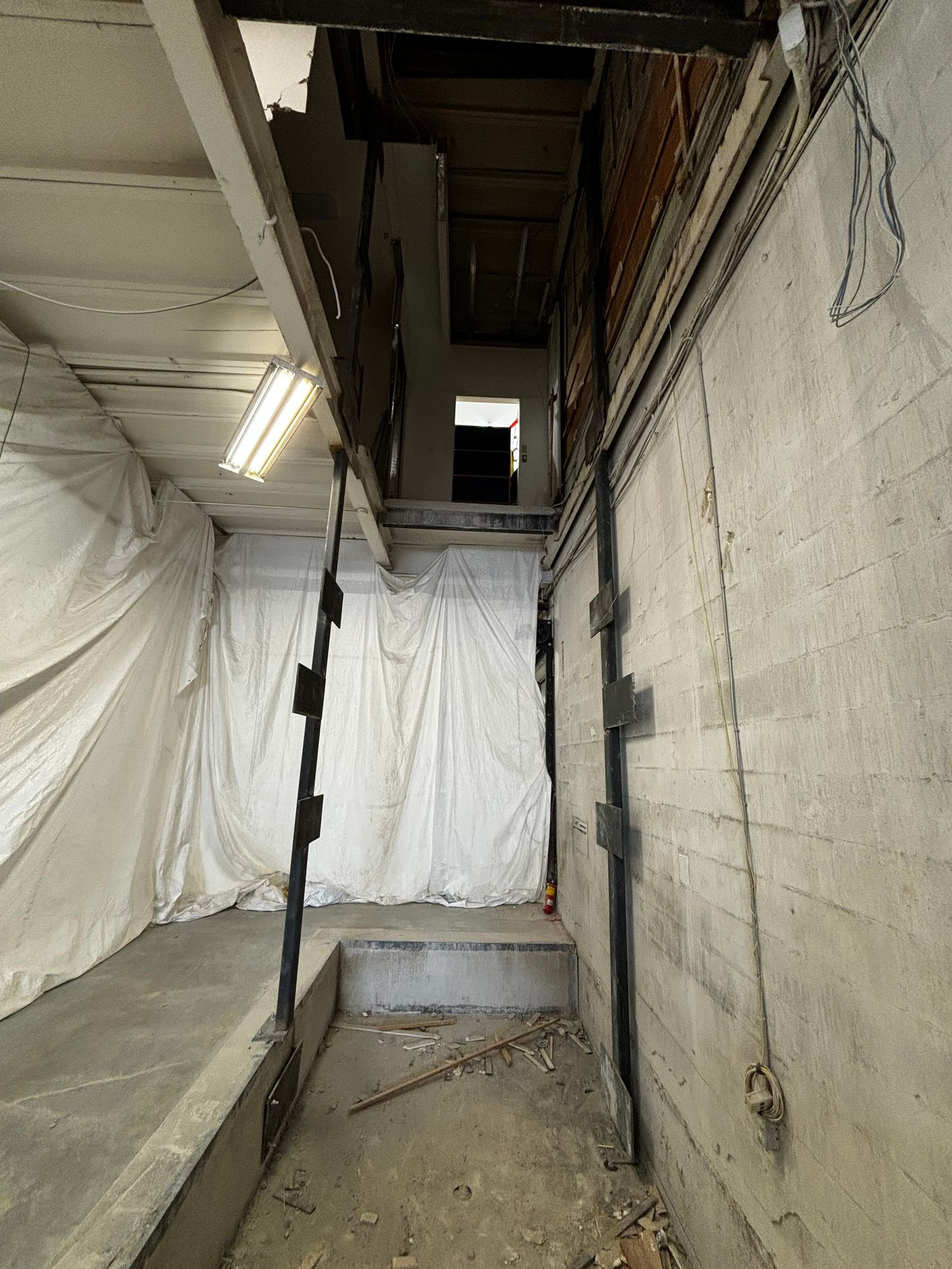 Intérieur du sous-sol avec briques et béton apparents. Un escalier mène à l'étage supérieur ; les supports sont visibles dans les murs.