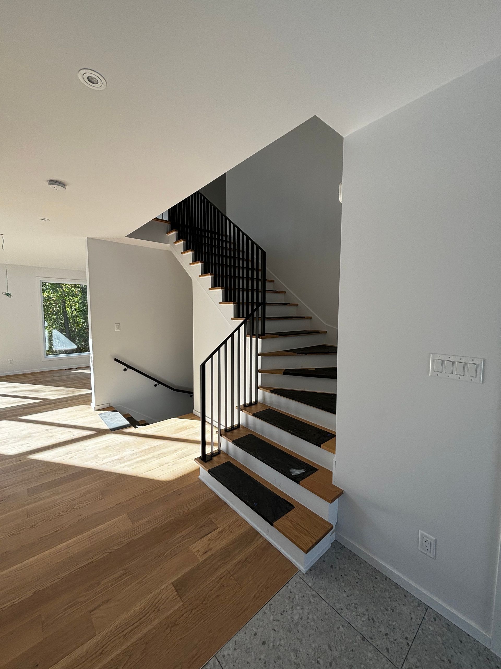 Vue intérieure d'un escalier récemment rénové avec rampes en fer noir, parquet et murs blancs.
