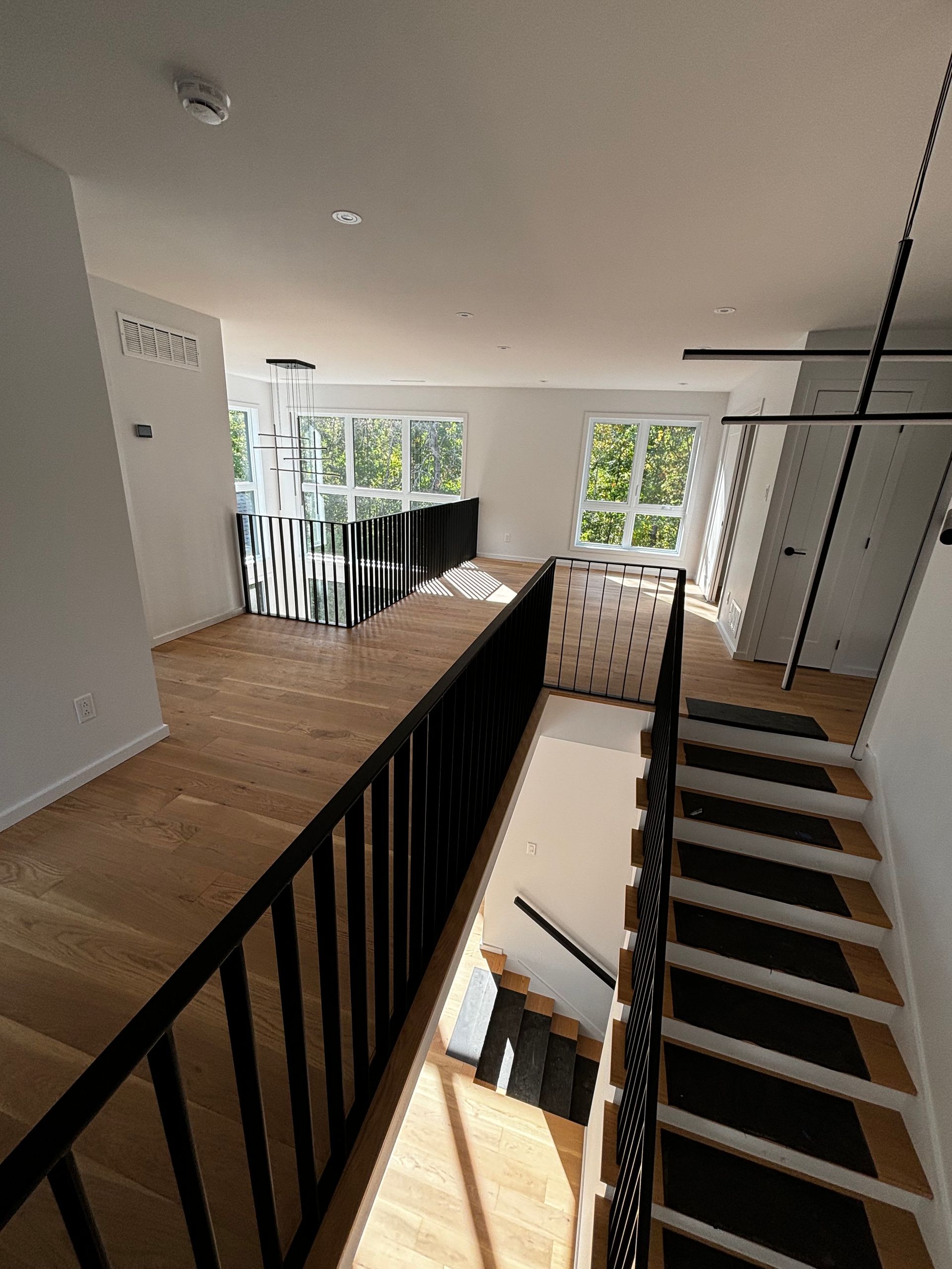 Vue intérieure d'une maison moderne avec un escalier, des rampes noires et un parquet.