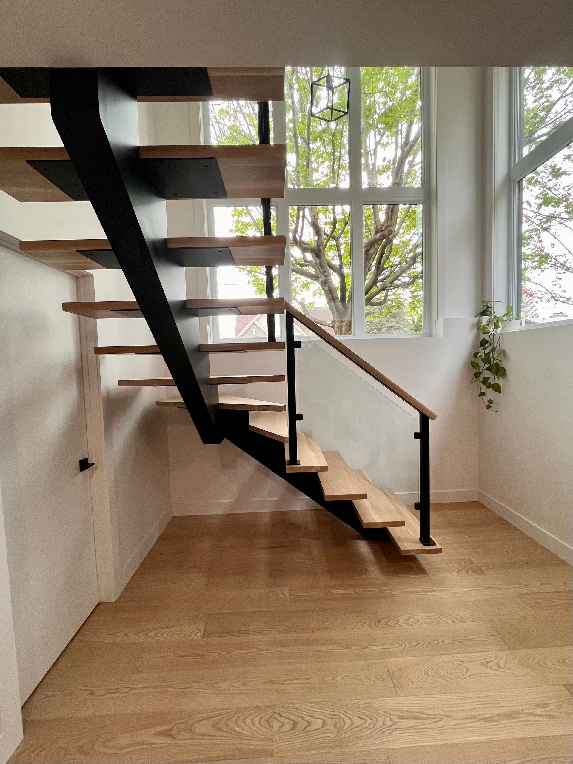 Escalier moderne en bois avec support en métal noir, près d'une fenêtre avec vue.