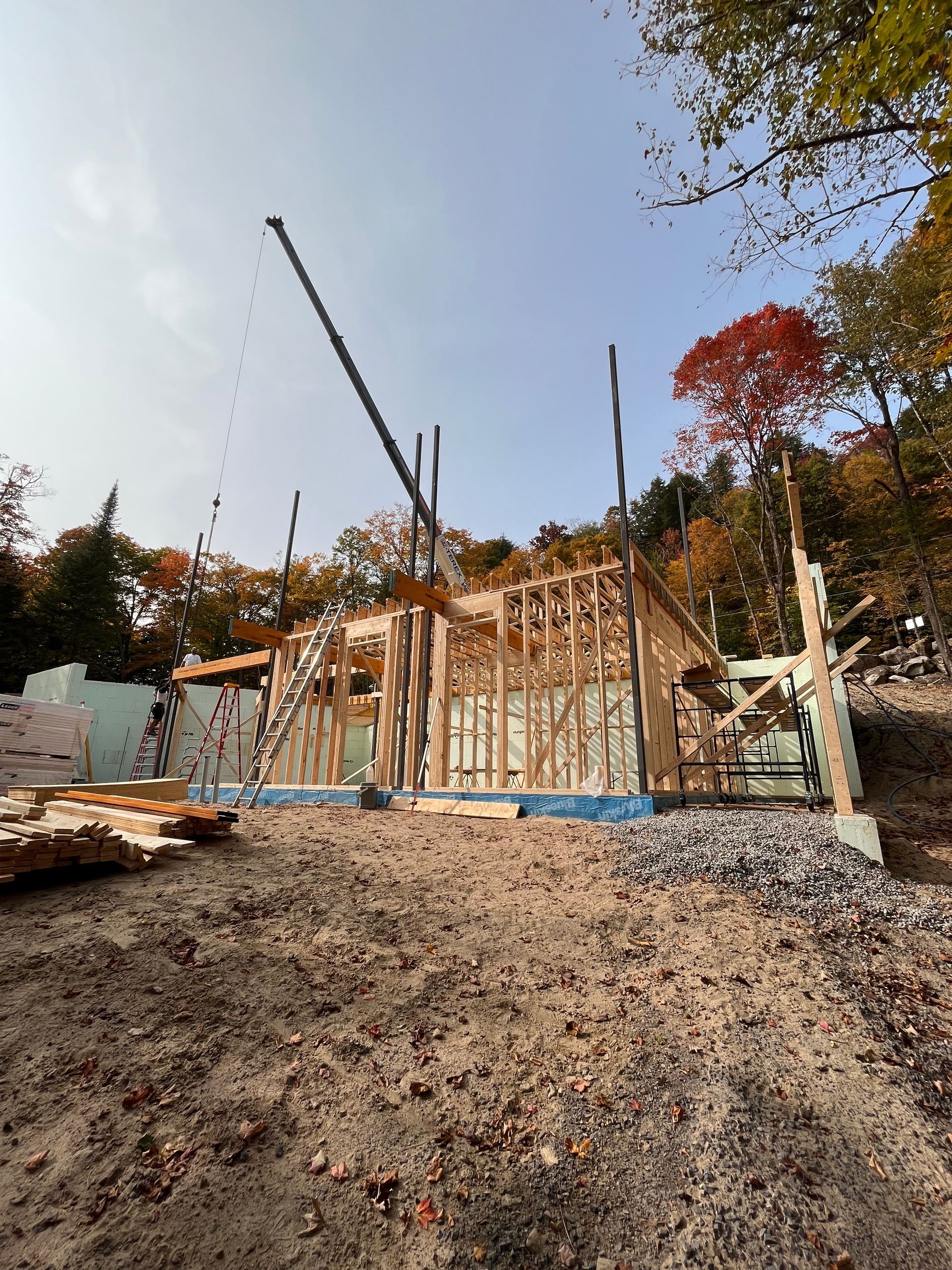 Construction d'un bâtiment à ossature bois ; bois apparent, partiellement achevé, sur un terrain vague, avec des arbres en arrière-plan.