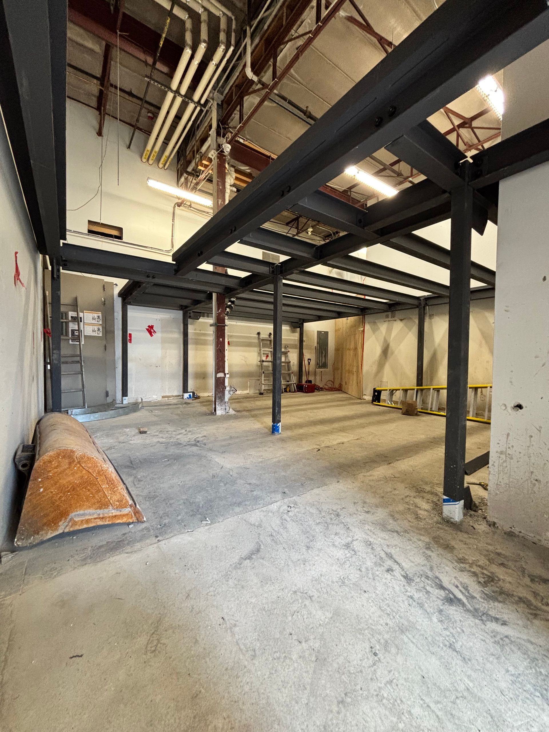 Espace industriel vide avec une structure métallique inachevée et un sol en béton.