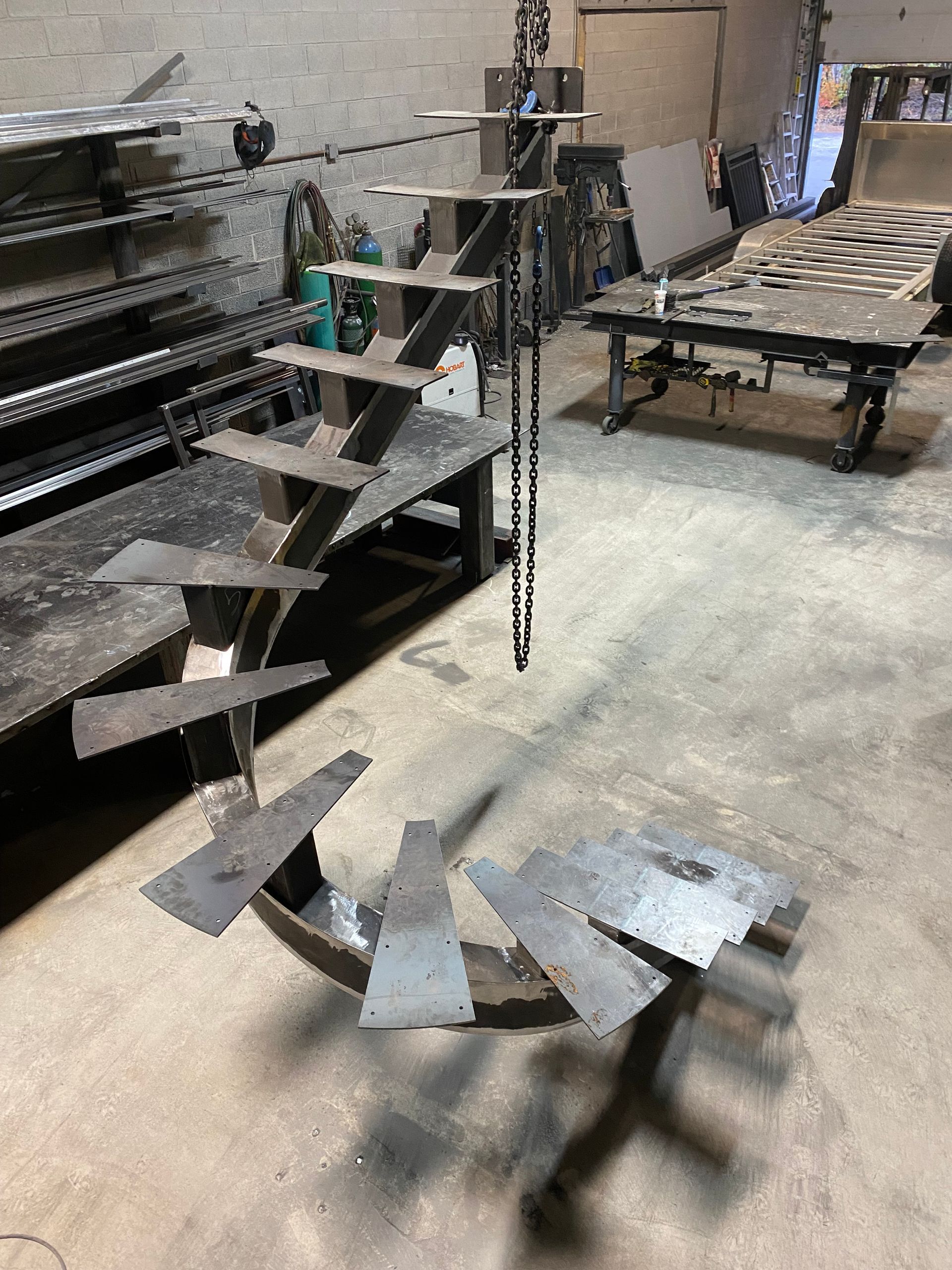 Escalier en colimaçon métallique dans un atelier, marches soudées sur un support central.