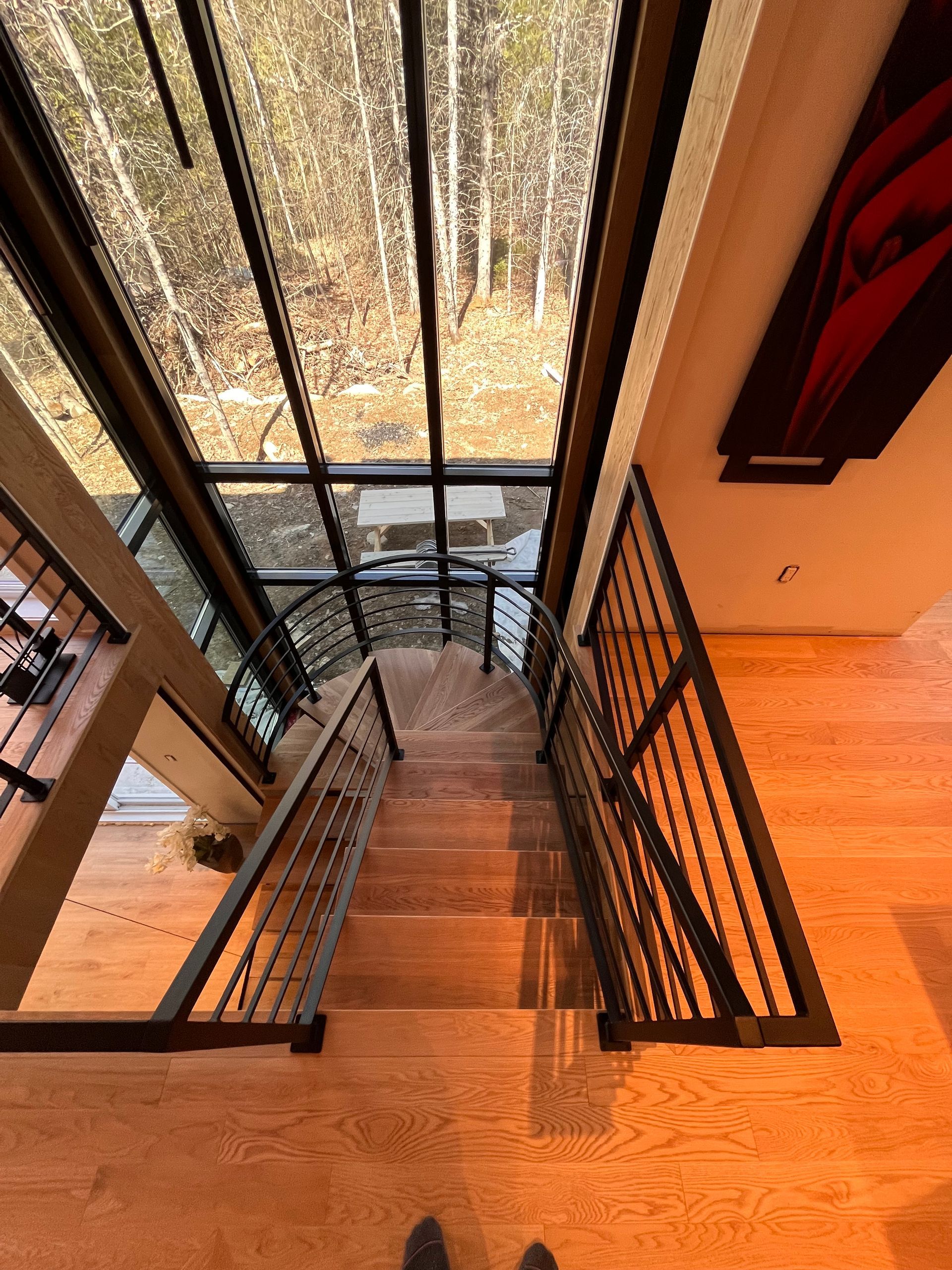 Escalier en bois avec rampes en métal et grande fenêtre donnant sur les arbres.