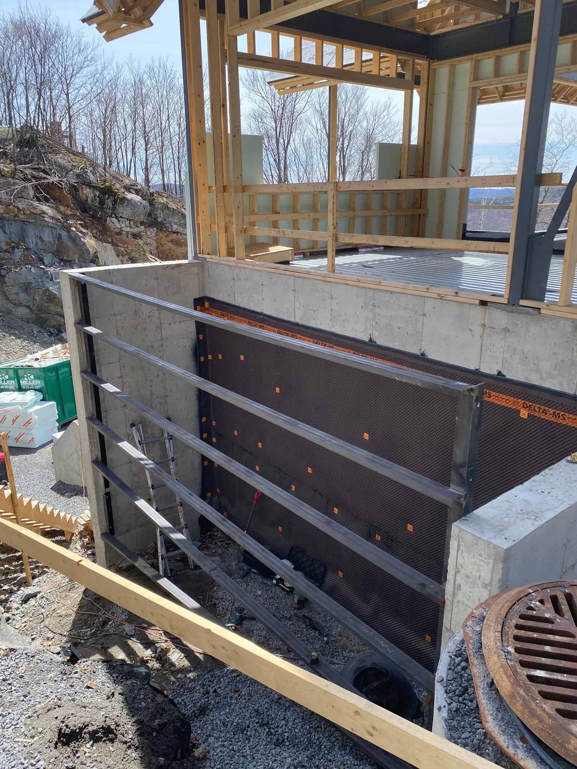 Mur de fondation en construction, membrane de drainage et ossature visibles.
