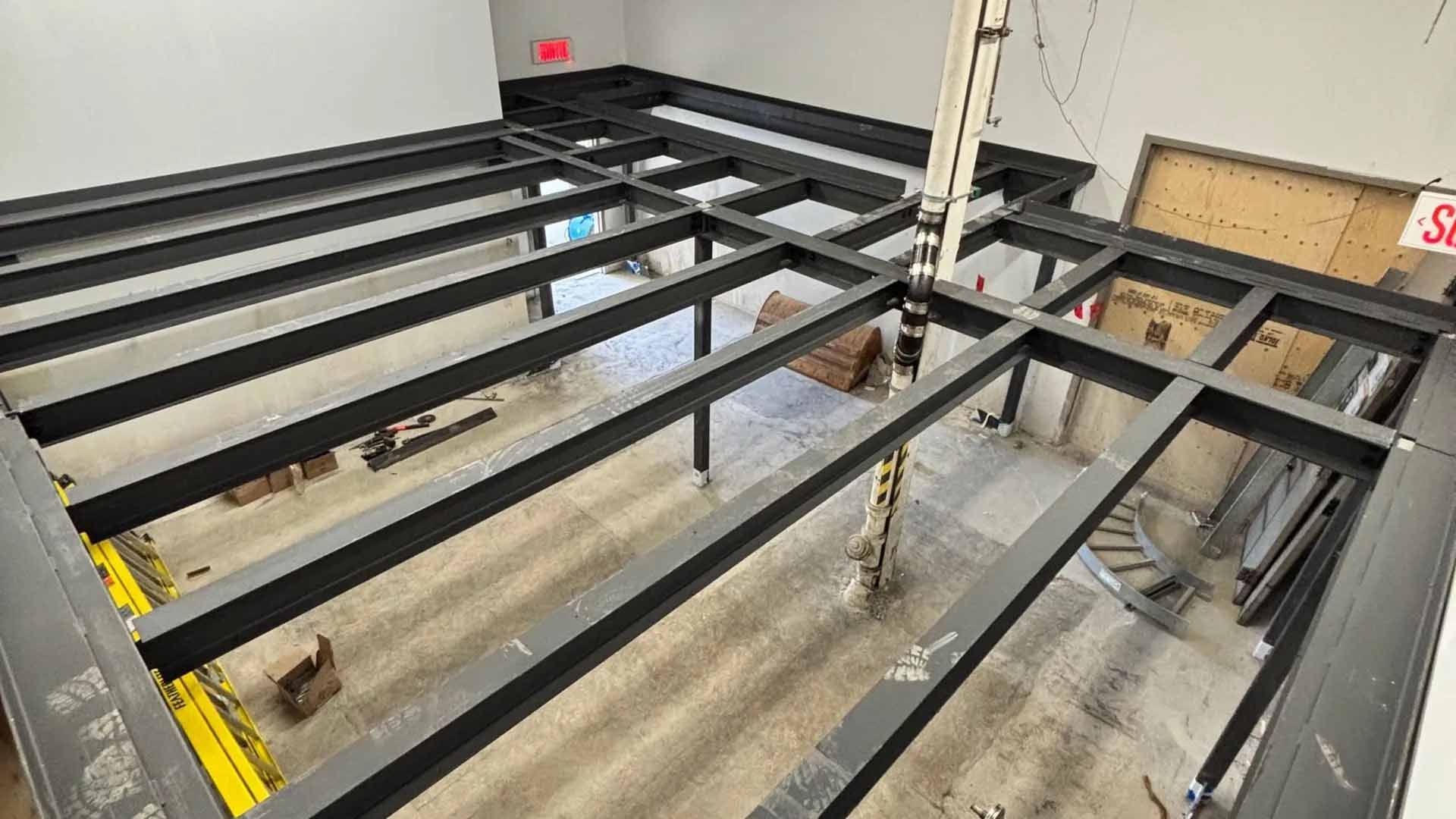 Vue aérienne d'une structure métallique noire en construction dans un espace au sol gris.