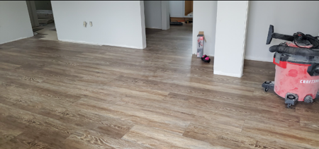 Newly installed wood-look laminate flooring in a room with white walls and a red shop vacuum cleaner.