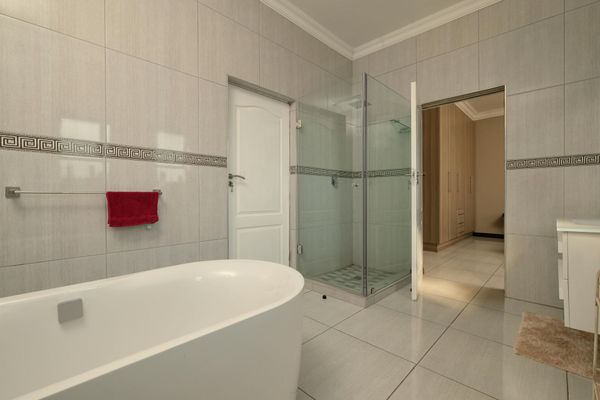 A bright, modern bathroom featuring a white freestanding bathtub, a glass-enclosed shower, and light-toned tiled walls.