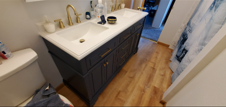 A navy blue double-sink bathroom vanity with gold hardware, white countertops, and a wood-look floor.