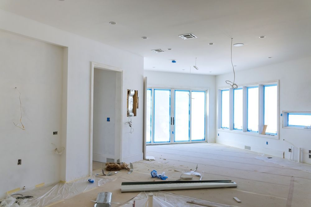 An unfinished interior room with white walls, recessed lighting, and large windows covered in blue protective film.