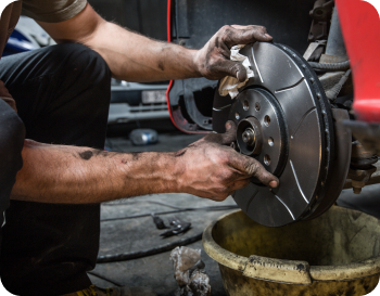 Mechanic holding a new brake rotor while working on a car in a garage, hands are dirty.