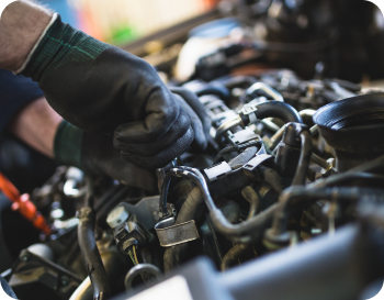 Hands in black gloves working on a car engine, inside a garage.