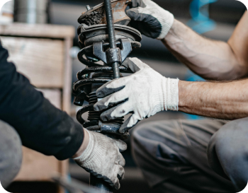 Two mechanics wearing gloves, handling a car shock absorber.