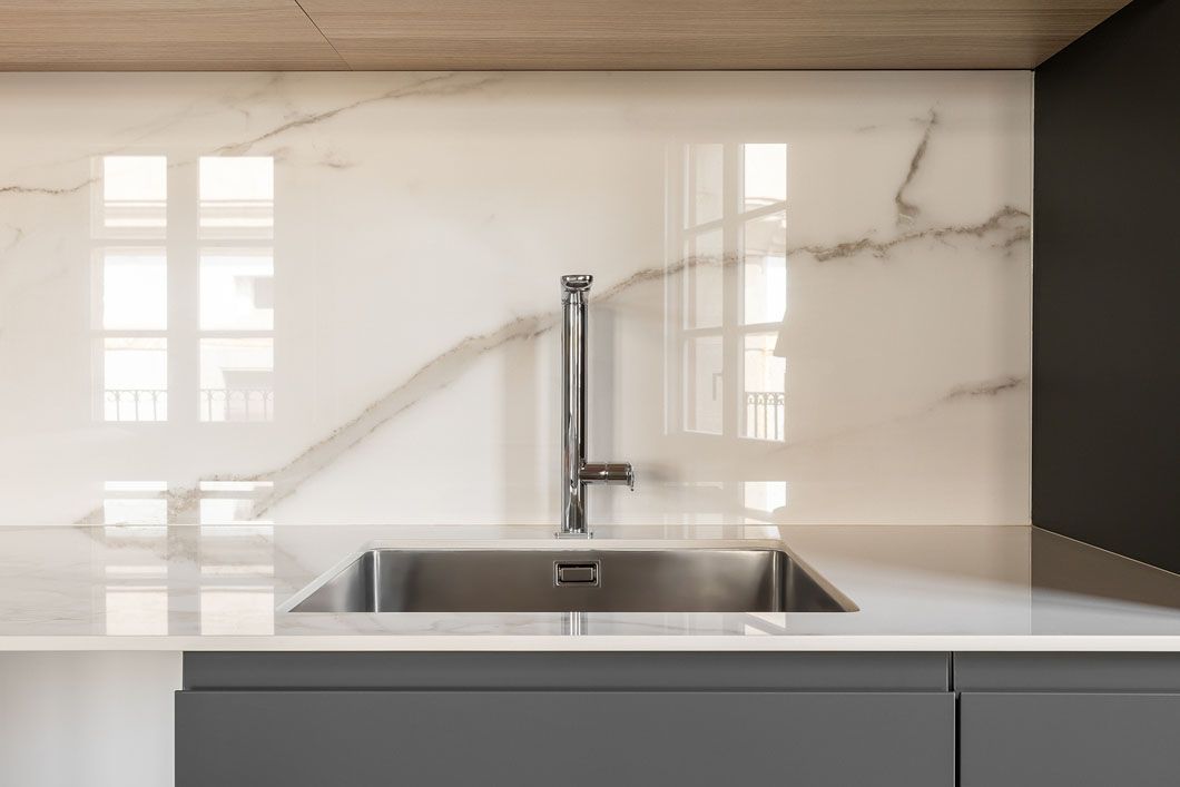 A kitchen sink with a faucet and a marble wall behind it.