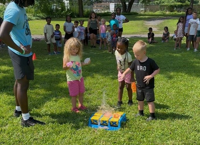 Children playing a game outdoors with a supervising adult.