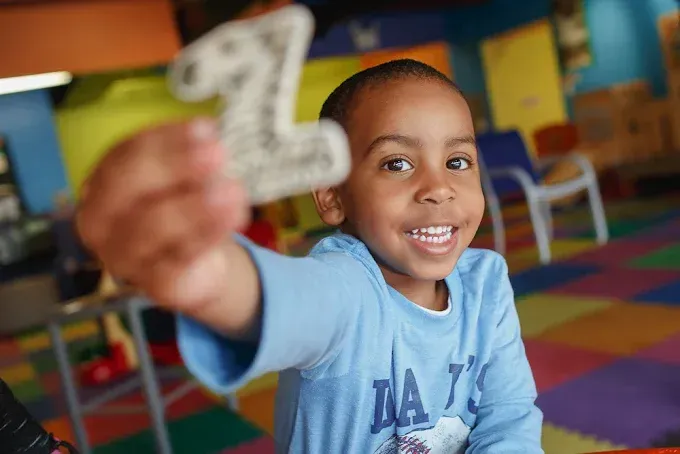 Children standing by white buckets in a sunny outdoor setting.