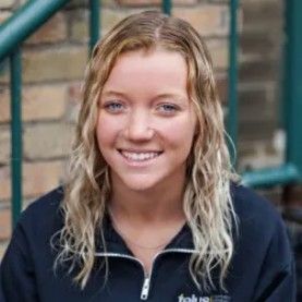 A young woman is smiling for the camera while sitting on a set of stairs.