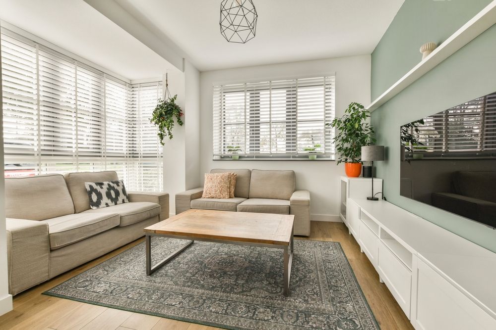 Bright modern living room with beige sofas, white blinds, gray rug, and wall-mounted TV