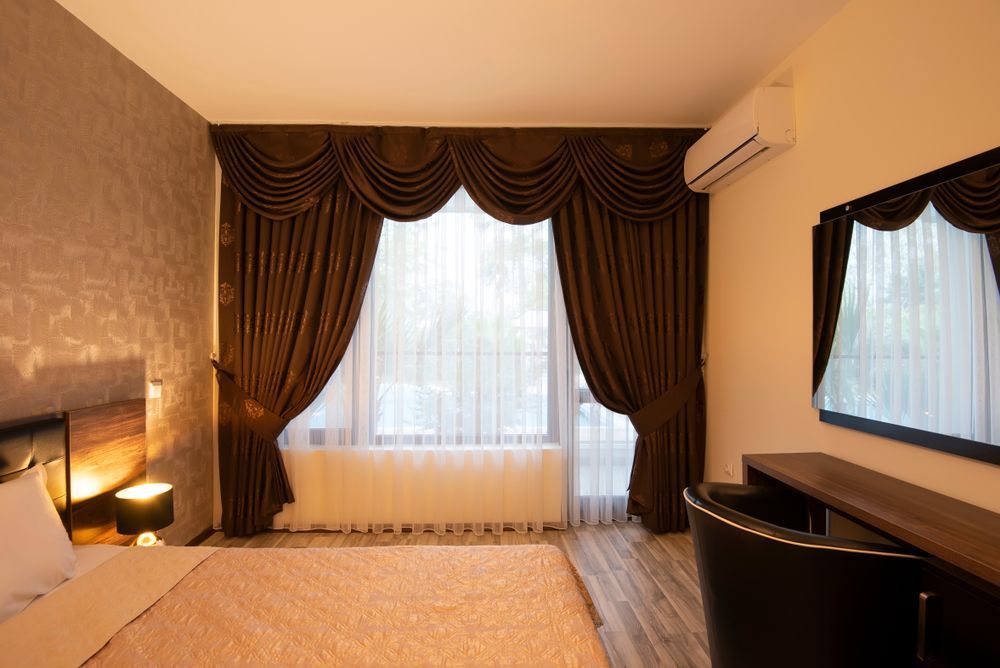 Elegant hotel bedroom with dark drapes, large window, bed, desk, and wall mirror