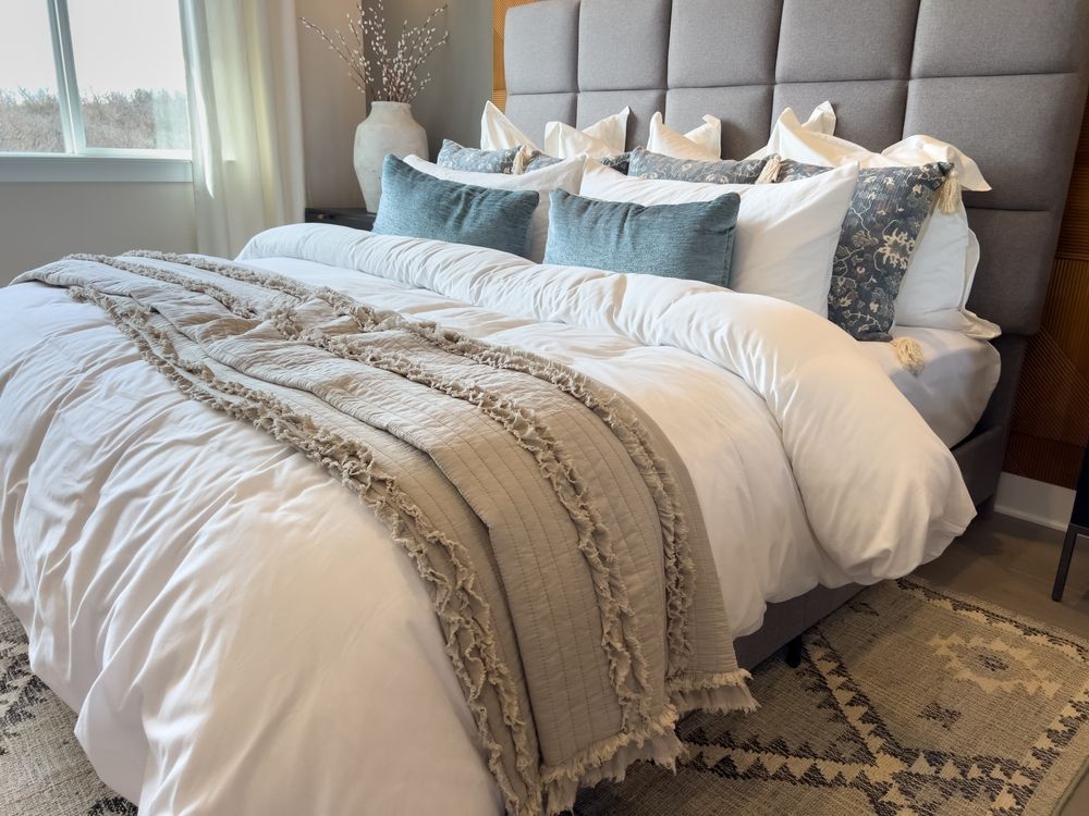 Cozy bedroom with gray tufted headboard, white bedding, blue pillows, and patterned throw blanket