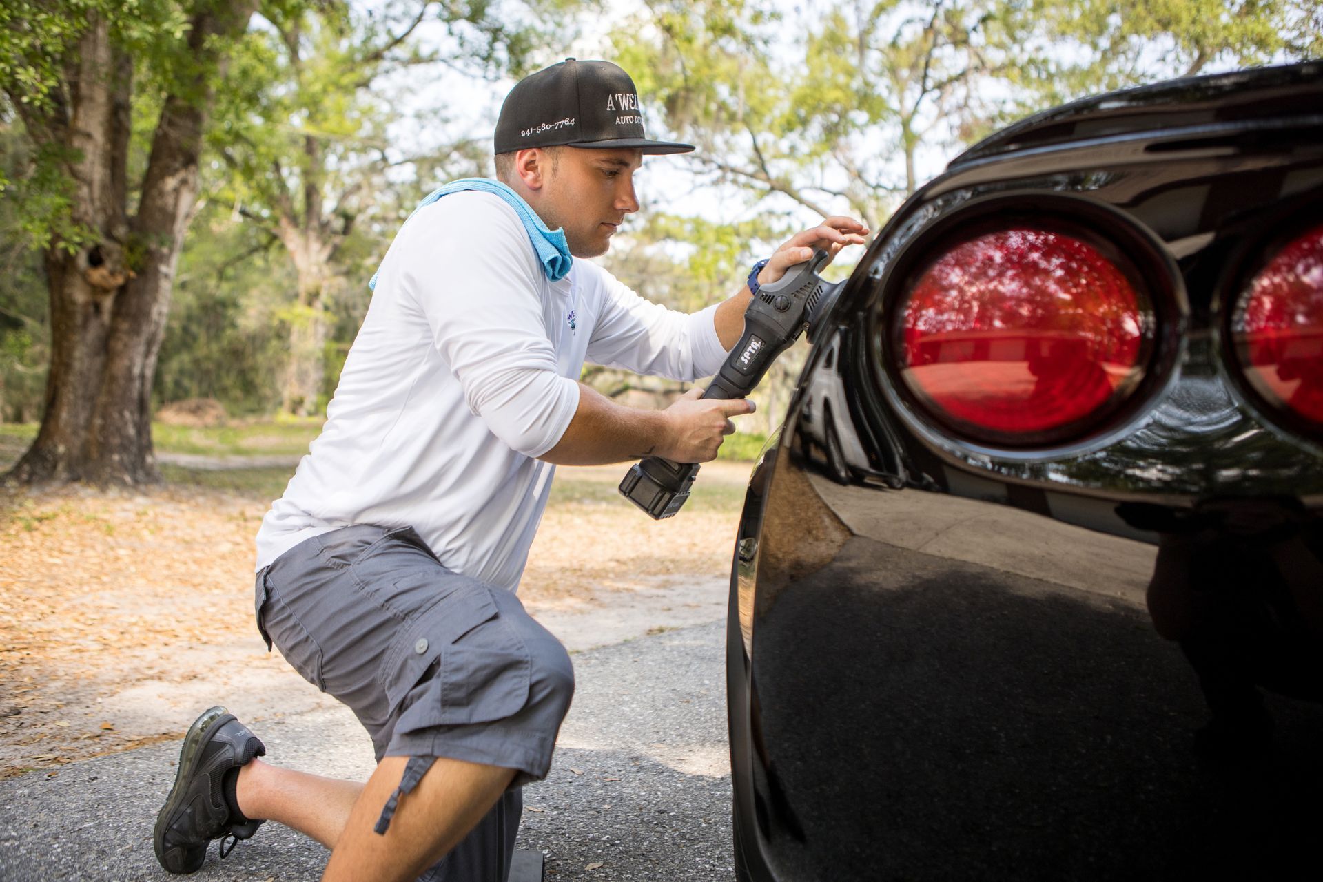 A man is kneeling down in front of a black car.