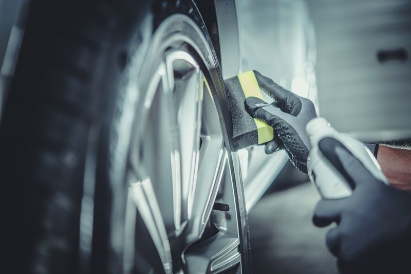 A person is cleaning a car wheel with a sponge and spray.