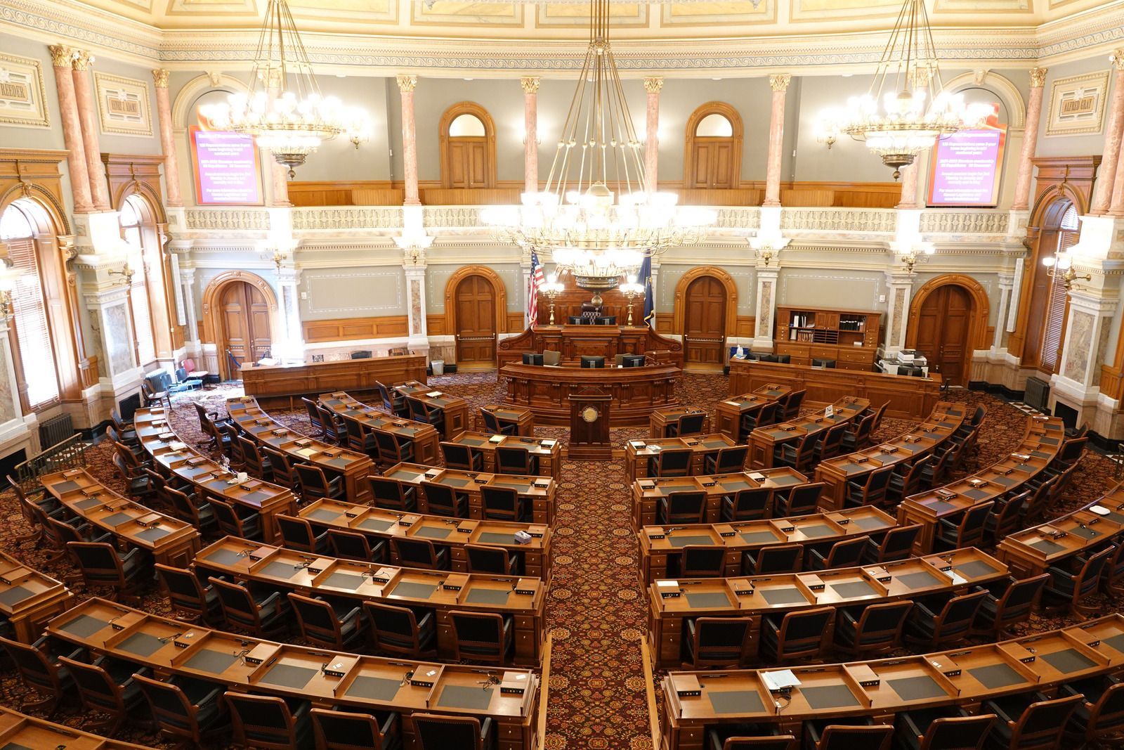 A large, ornate legislative chamber with rows of desks, adorned with chandeliers, and a central dais.
