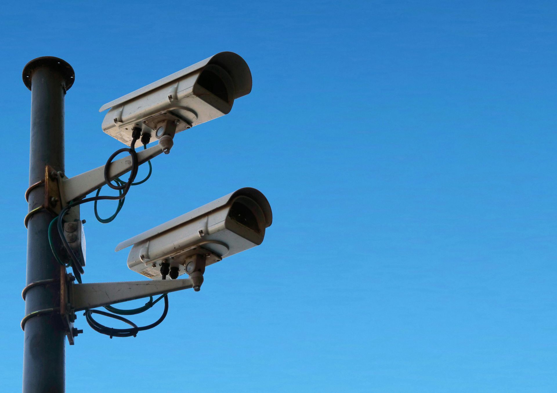 Two security cameras mounted on a pole against a clear blue sky.