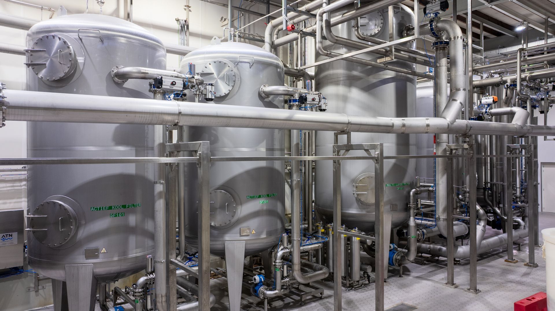 Een rij roestvrijstalen tanks en leidingen in een fabriek.