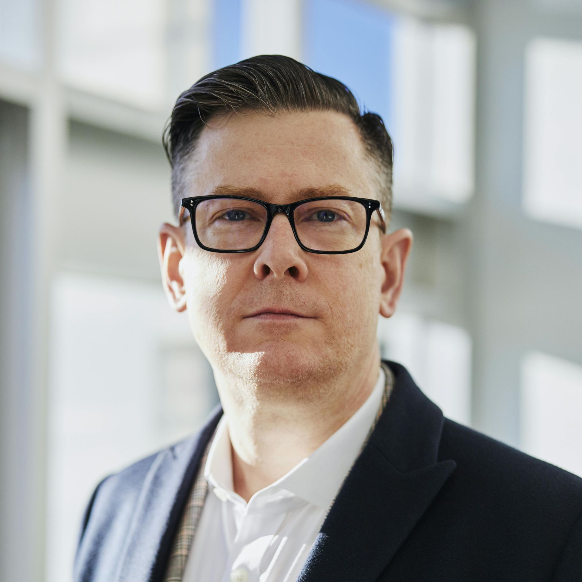 A man wearing glasses and a suit looks at the camera