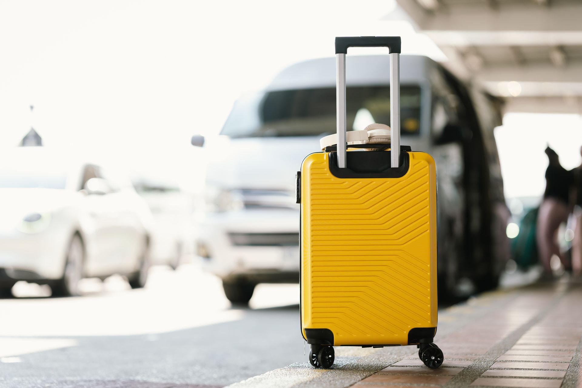 Yellow wheeled suitcase at a curb with cars and a van in the background