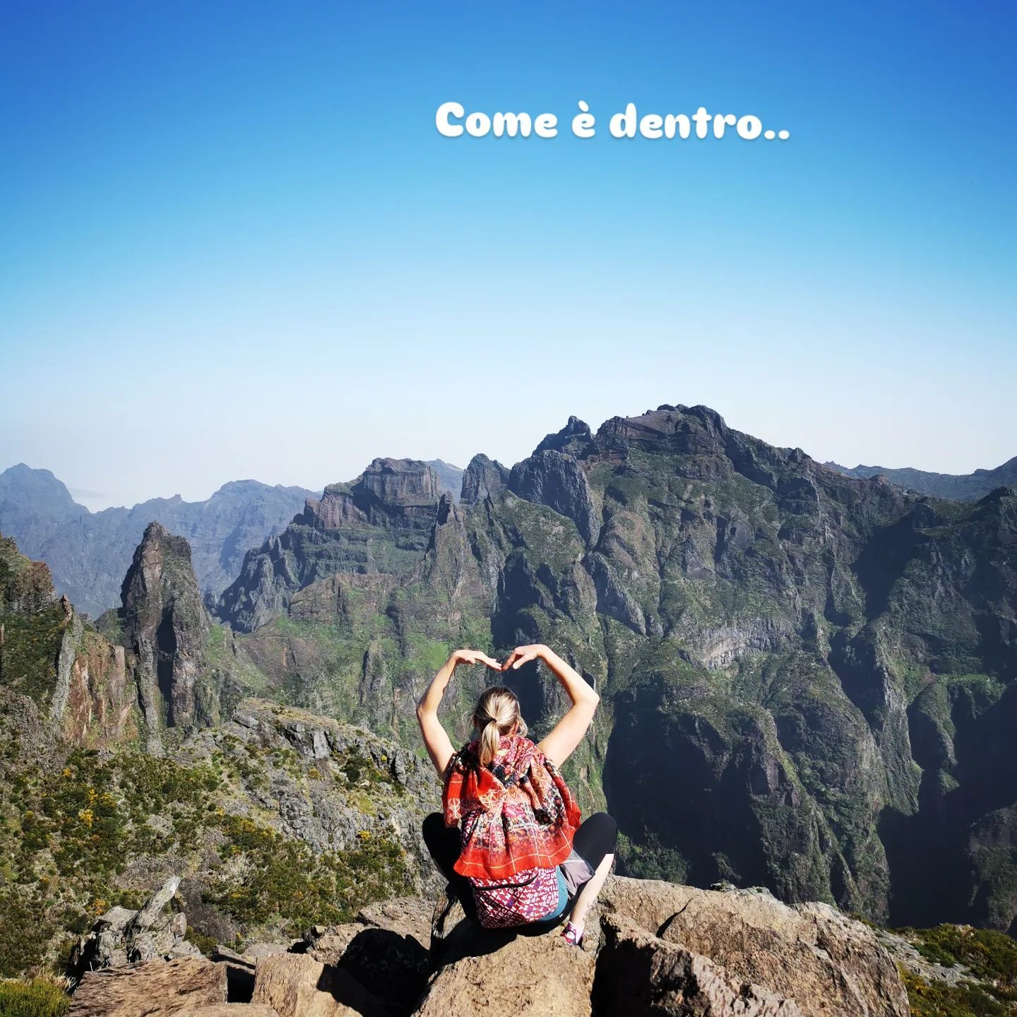 Donna che forma un cuore con le mani davanti a una catena montuosa, il testo sopra recita