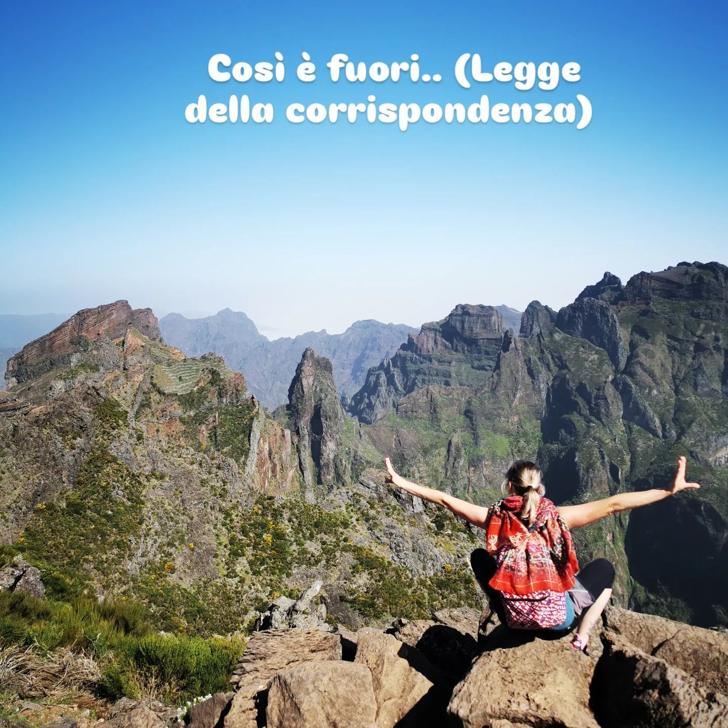 Donna con le braccia tese in cima a una montagna, contro un paesaggio aspro e un cielo azzurro. Testo in italiano sopra.